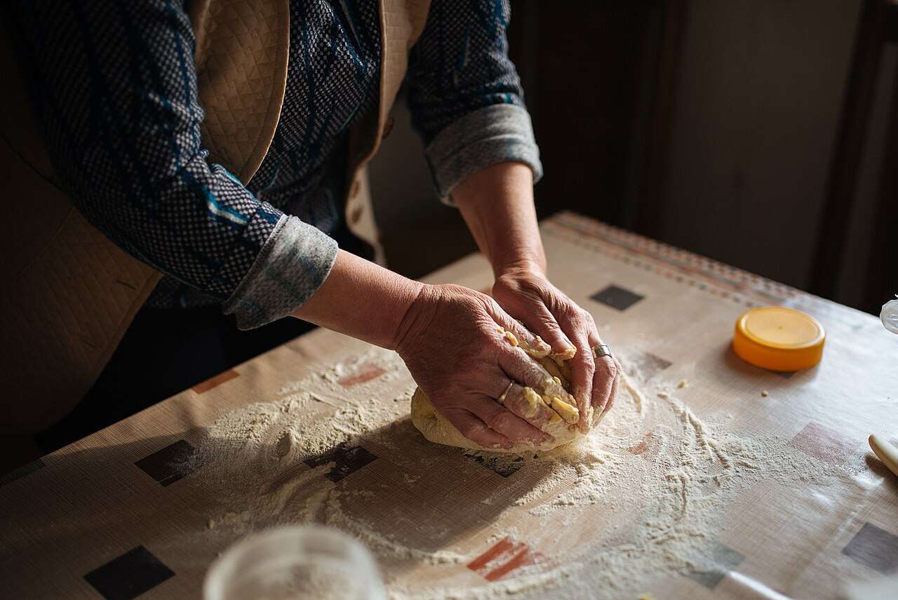 Manos de panadera amasando pan sobre una mesa enharinada en un obrador