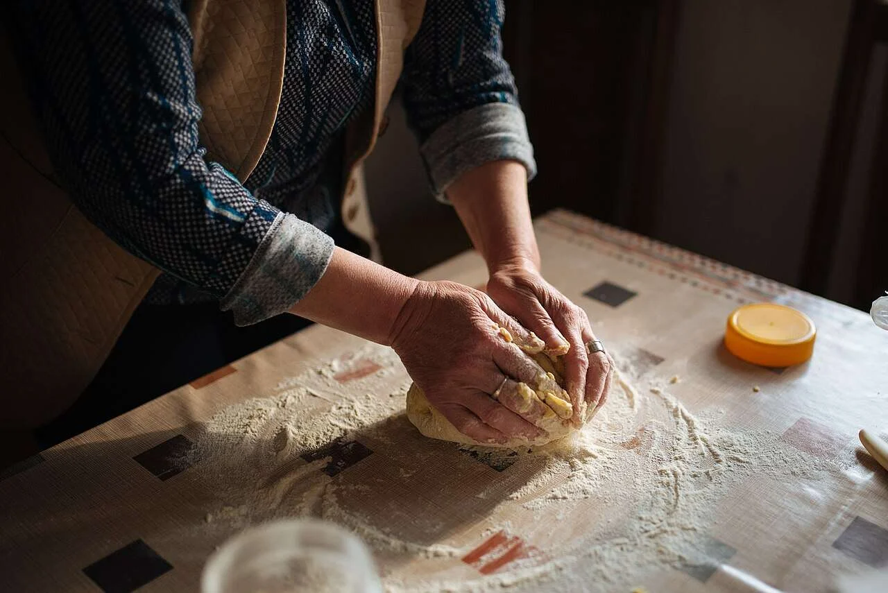Manos de panadera amasando pan sobre una mesa enharinada en un obrador