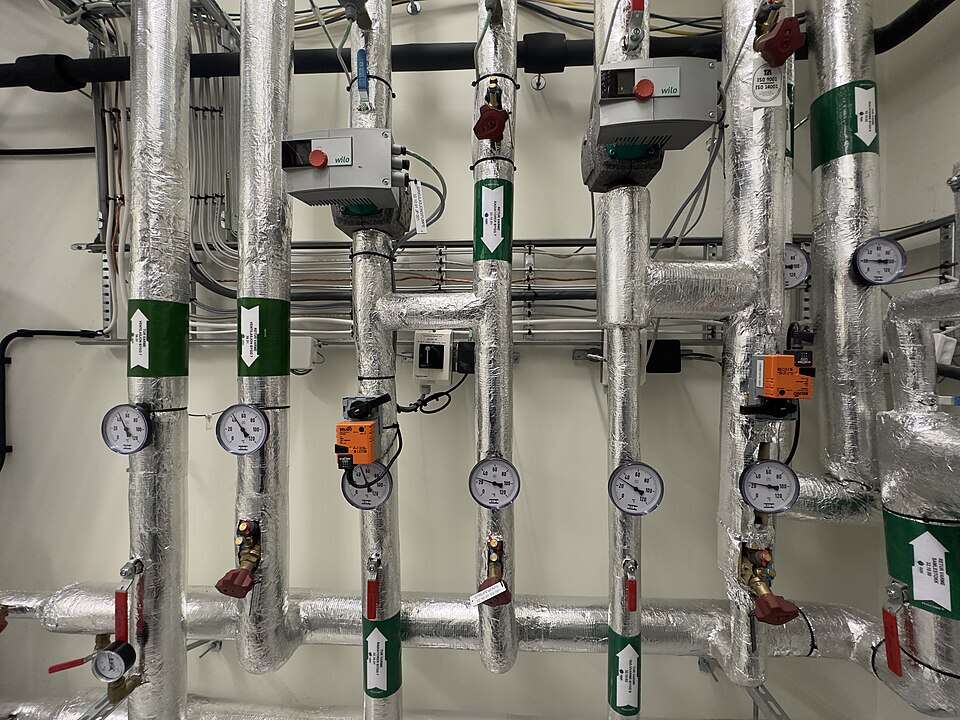 Colector de agua caliente sanitaria con termómetros y bombas de recirculación en la sala de máquinas de un edificio