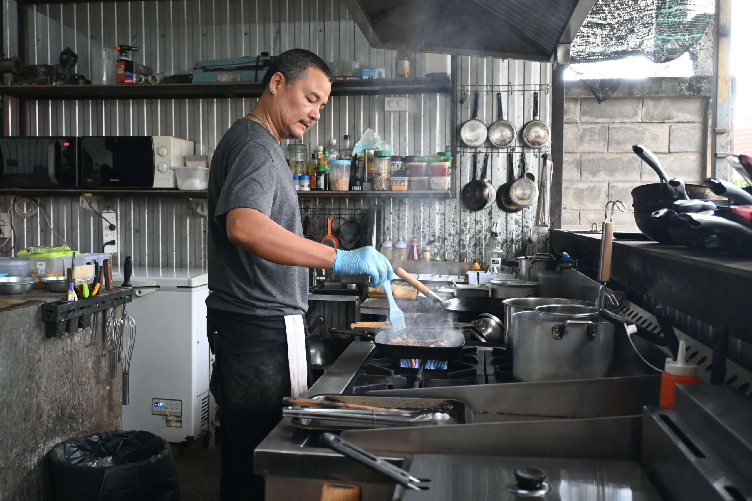 Cocinero con guante desechable salteando en un fuego de una cocina profesional