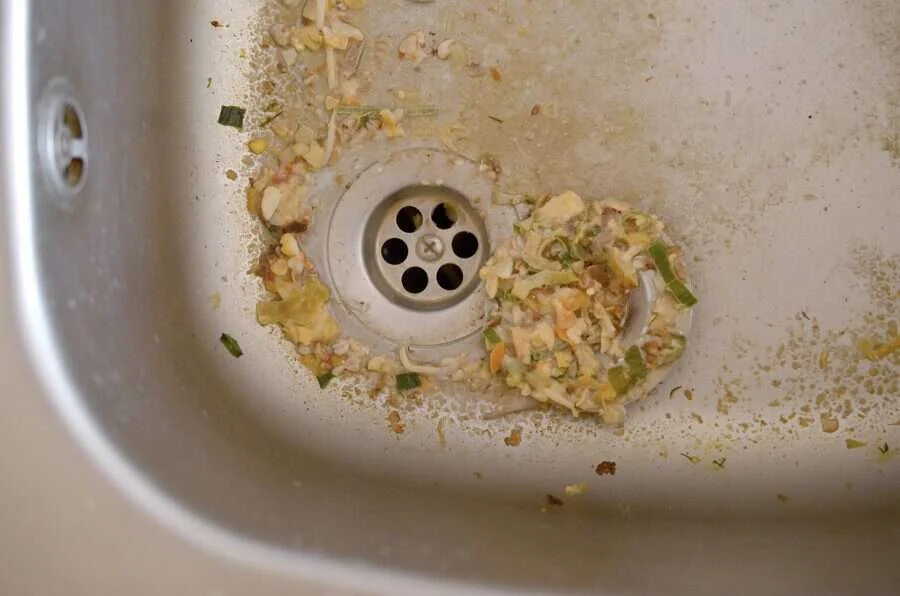 Rejilla de un fregadero rodeada de restos de comida acumulados